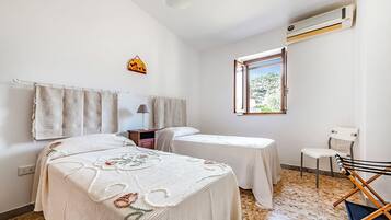 A room with two beds, a window, an air conditioner, a desk, and a chair.