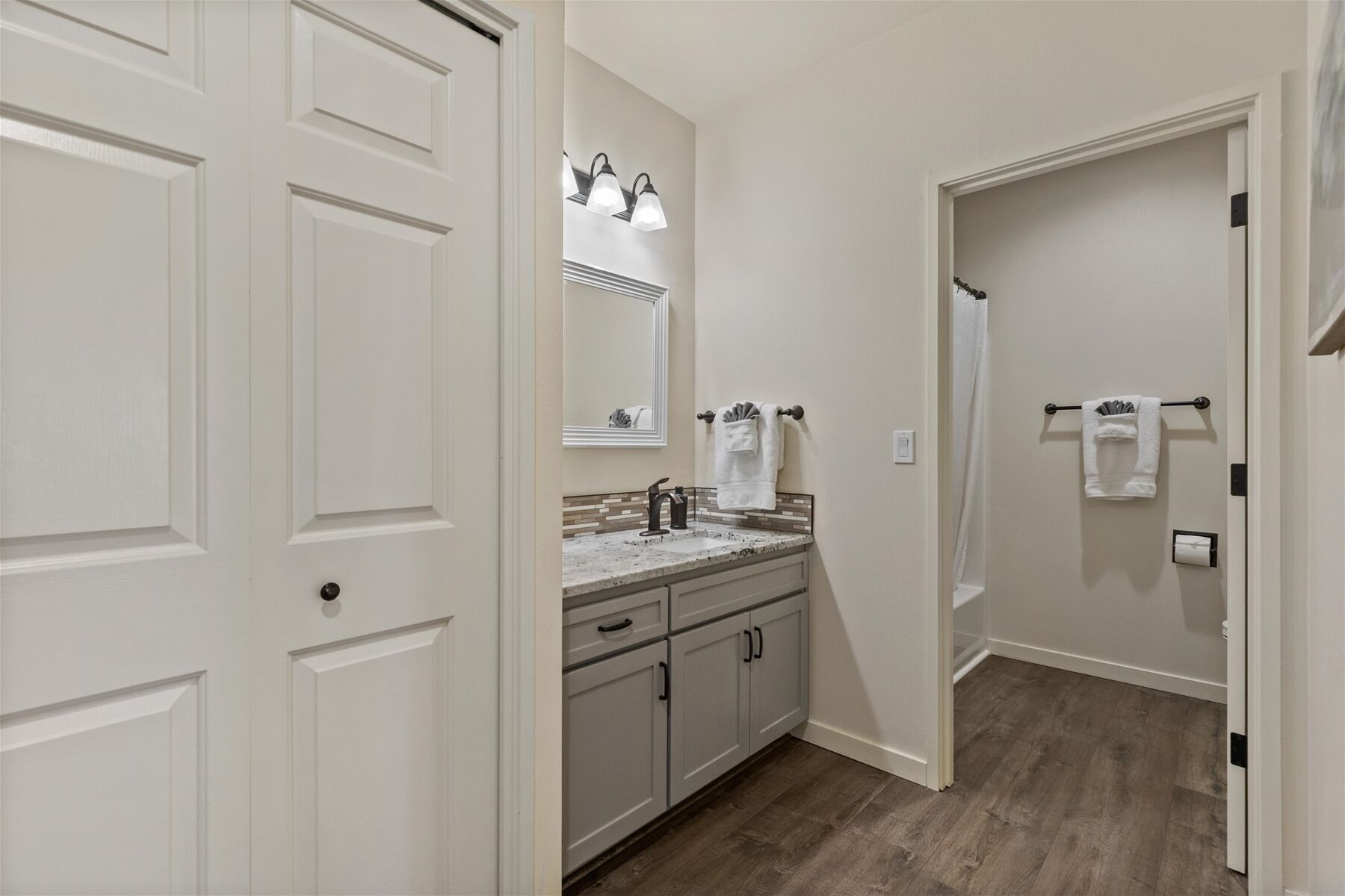 A bathroom with a sink, mirror, towel rack, and wooden flooring.