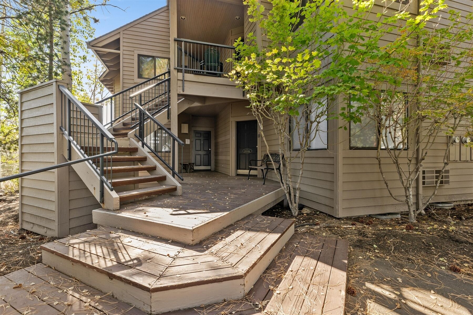 A two-story building with a wooden deck, a staircase, and a small outdoor seating area.