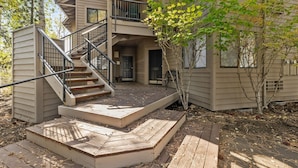 A two-story building with a wooden deck, a staircase, and a small outdoor seating area. - New! Deschutes River Escape with Hot Tub & Views (Bend)