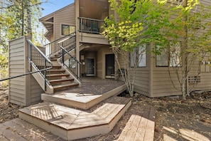 A two-story building with a wooden deck, a staircase, and a small outdoor seating area. - New! Deschutes River Escape with Hot Tub & Views (Bend)