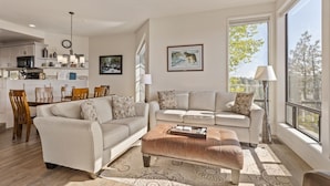 A modern living room with a sofa, ottoman, and dining area. - New! Deschutes River Escape with Hot Tub & Views (Bend)