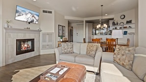 A living room with a fireplace, a sofa set, a coffee table, and a dining area with chairs and a table. - New! Deschutes River Escape with Hot Tub & Views (Bend)