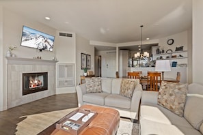 A living room with a fireplace, a sofa set, a coffee table, and a dining area with chairs and a table. - New! Deschutes River Escape with Hot Tub & Views (Bend)