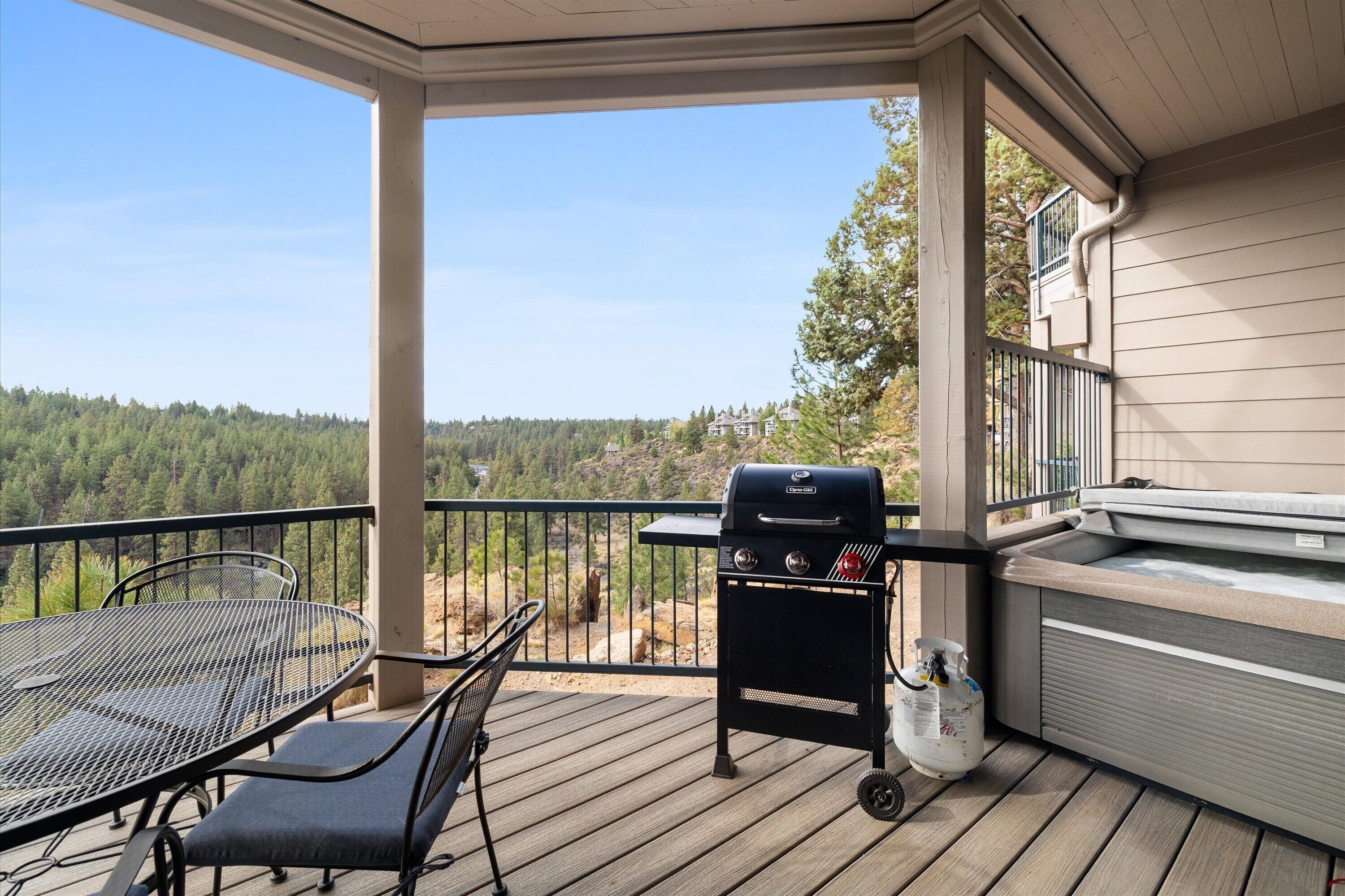 A covered outdoor area with a grill, seating, and a view of a forested landscape.