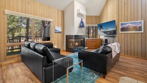 A modern living room with leather sofas, a glass coffee table, a fireplace, and wooden walls. - New! Cozy Bend Escape | Hot Tub | Forest Views (Bend)