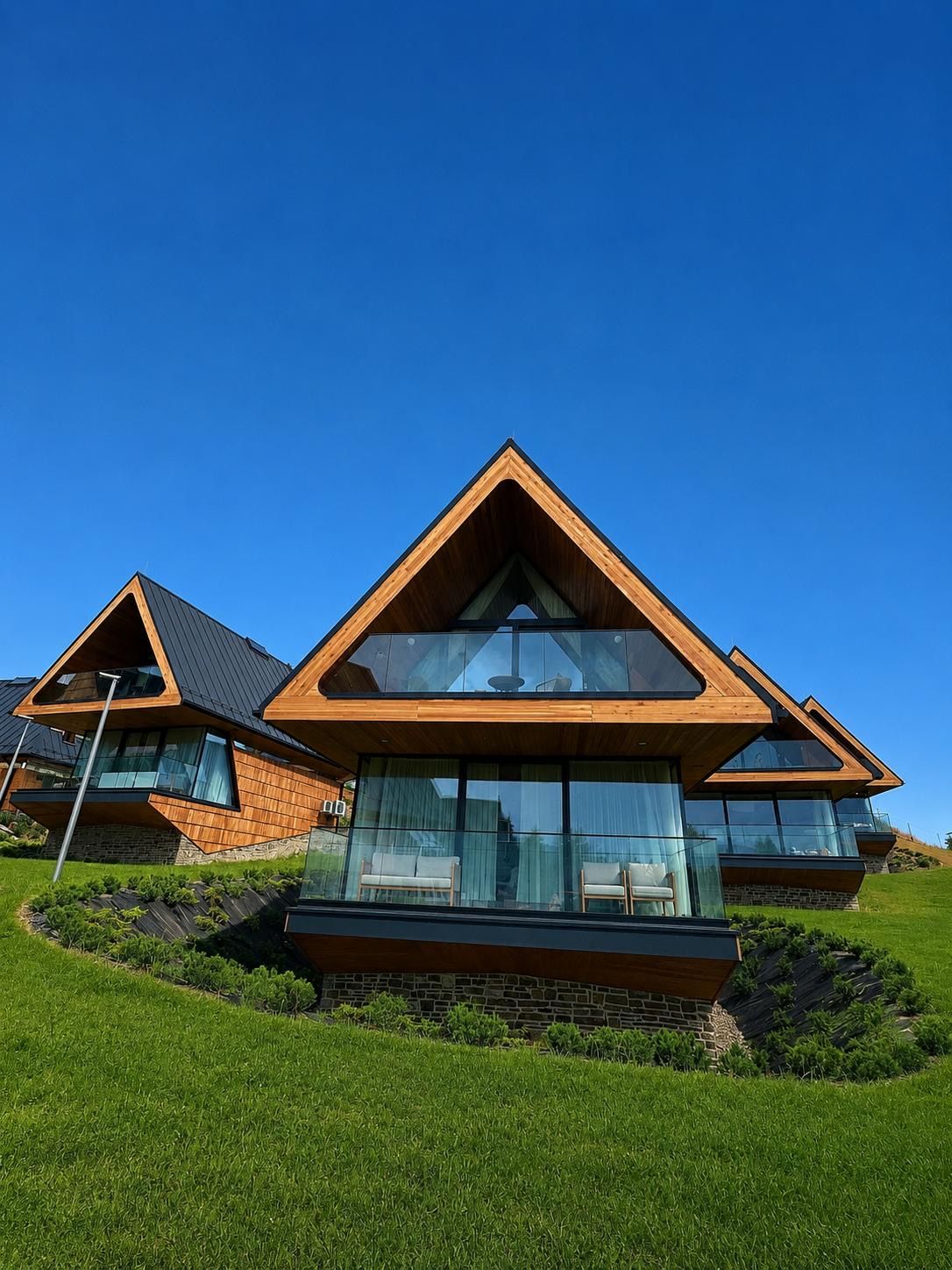 Una casa moderna con un diseño de techo triangular, ventanas grandes y un cimiento de piedra.
