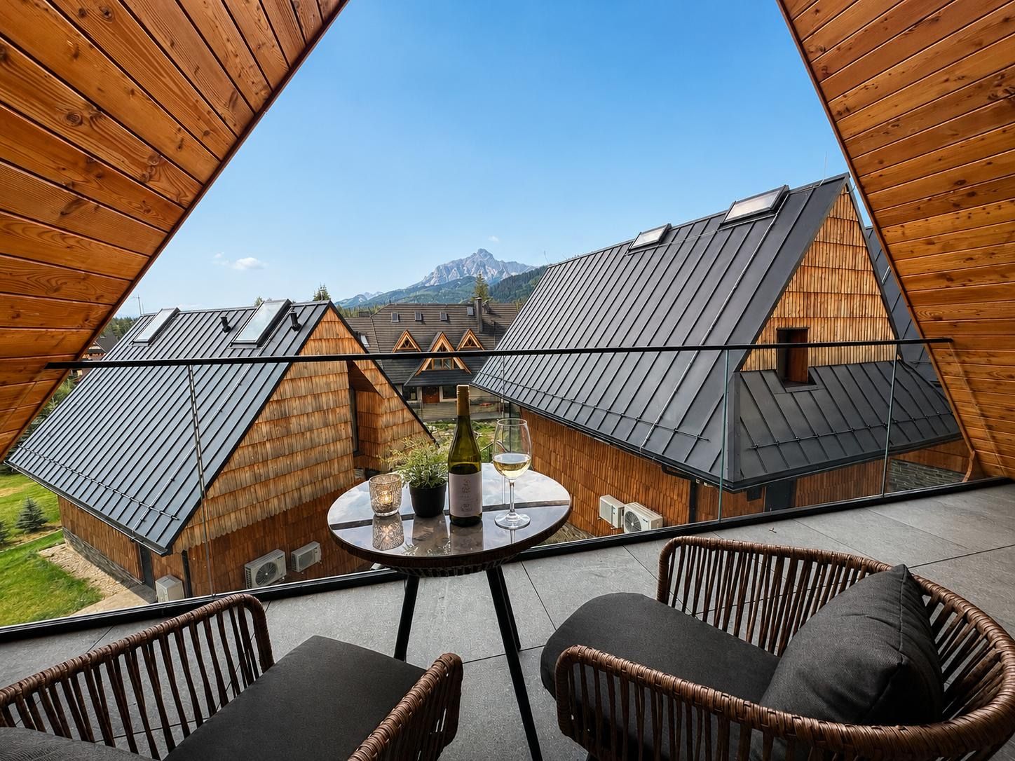A modern chalet with a panoramic view of mountains, furnished with wicker chairs and a table.