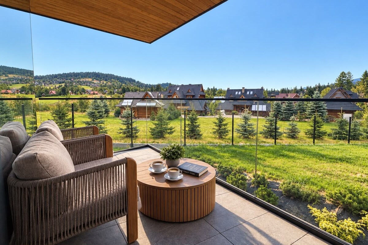 Un balcon doté d’un plafond en bois, une table ronde en bois avec deux tasses et un livre, et un fauteuil rembourré.