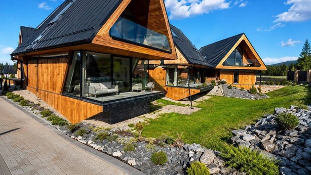 A modern wooden house with large windows and a sloped roof.