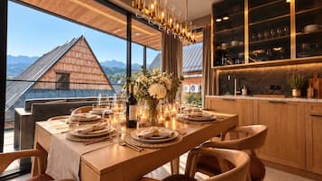 A dining area with a wooden table set for a meal, a chandelier, and a view of mountains through large windows.
