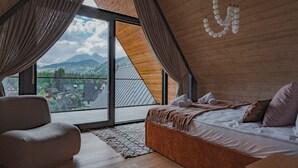 A bedroom with a large window, a bed, a chair, and a view of mountains.