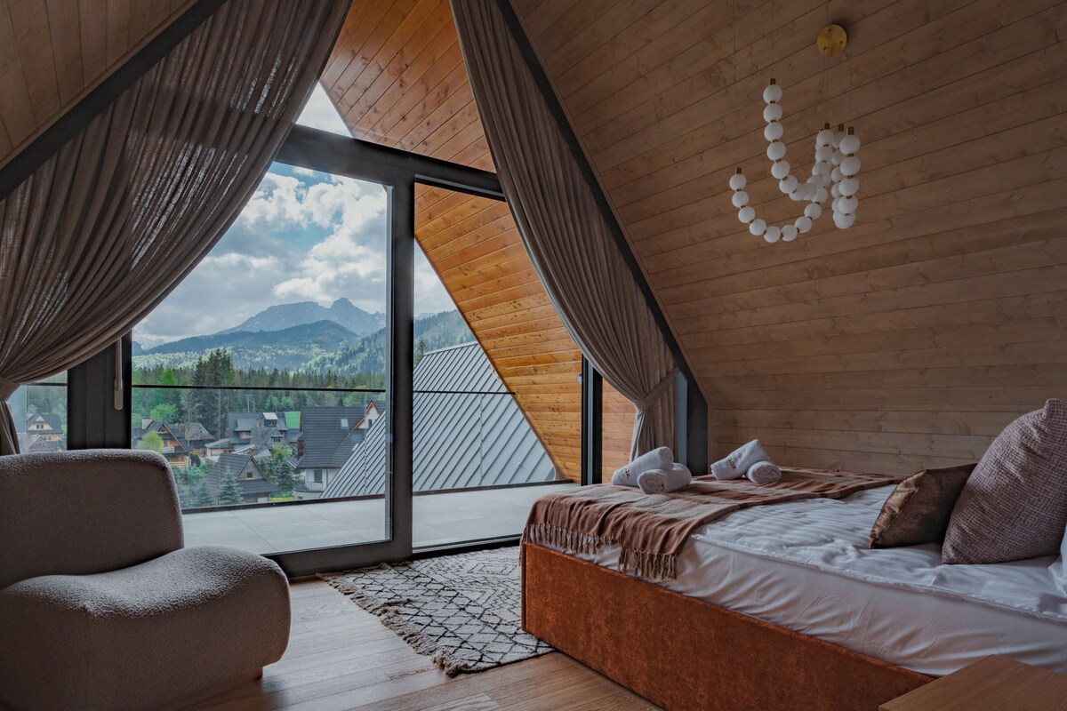 Une chambre avec une grande fenêtre, un lit, une chaise et une vue sur les montagnes.