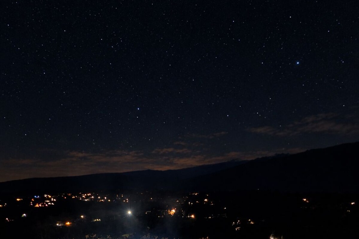 A hot tub with blue LED lights on a brick patio, overlooking a night sky with stars and a distant cityscape.