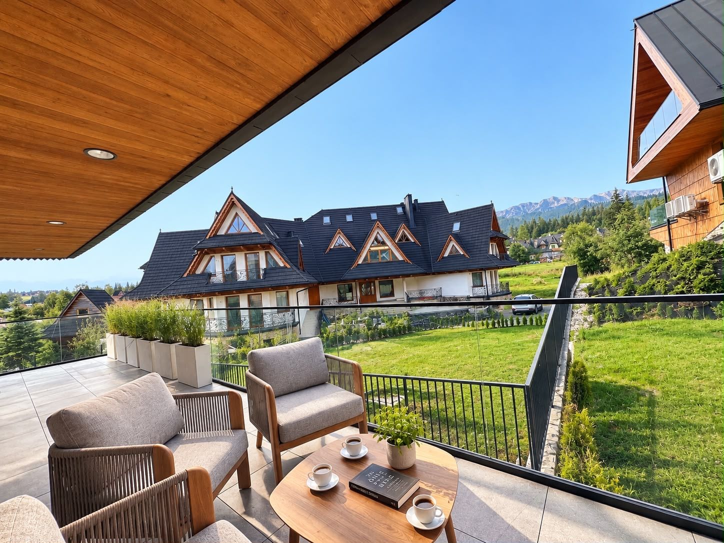 A modern outdoor seating area with a view of a large house and mountains in the background.