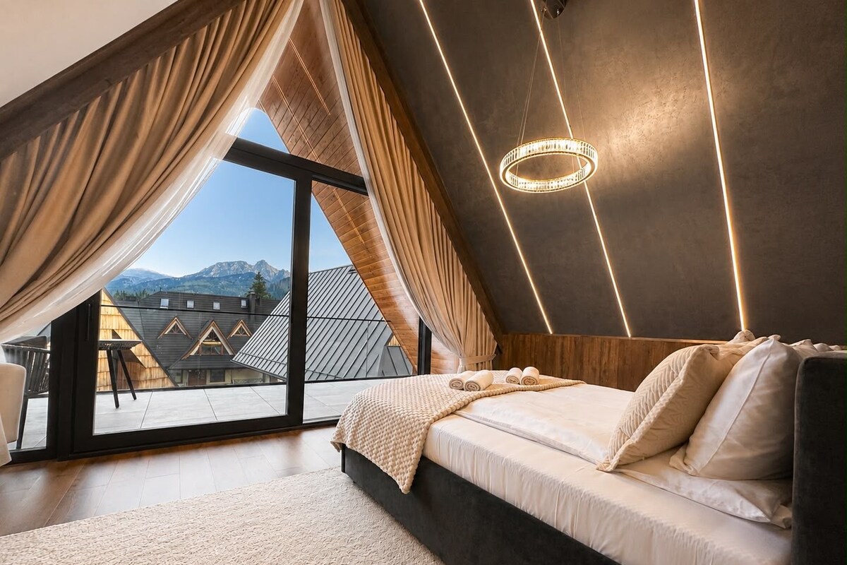 Une chambre dotée d’un grand lit, offrant une vue sur les montagnes, et présentant un design moderne au niveau du plafond.