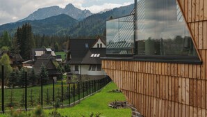 A modern house with a large glass window, wooden exterior, and a view of mountains.