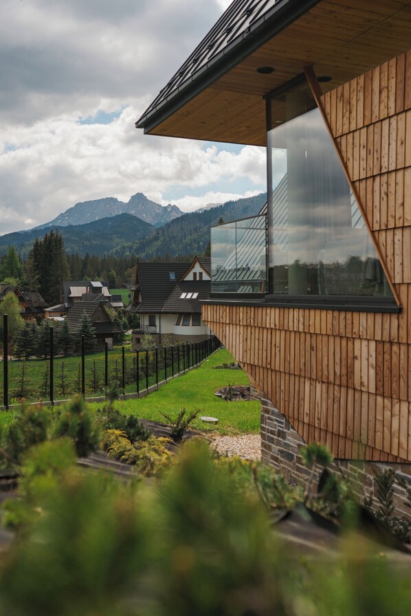 A modern house with a large glass window, wooden exterior, and a view of mountains.