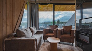 A modern living room with a sofa, armchairs, a coffee table, a fireplace, and a large window with a mountain view.