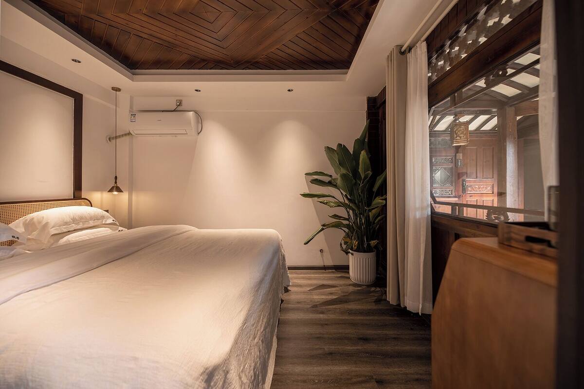 Ein Schlafzimmer mit einem Bett, einer Topfpflanze und einem Fenster mit Vorhängen.