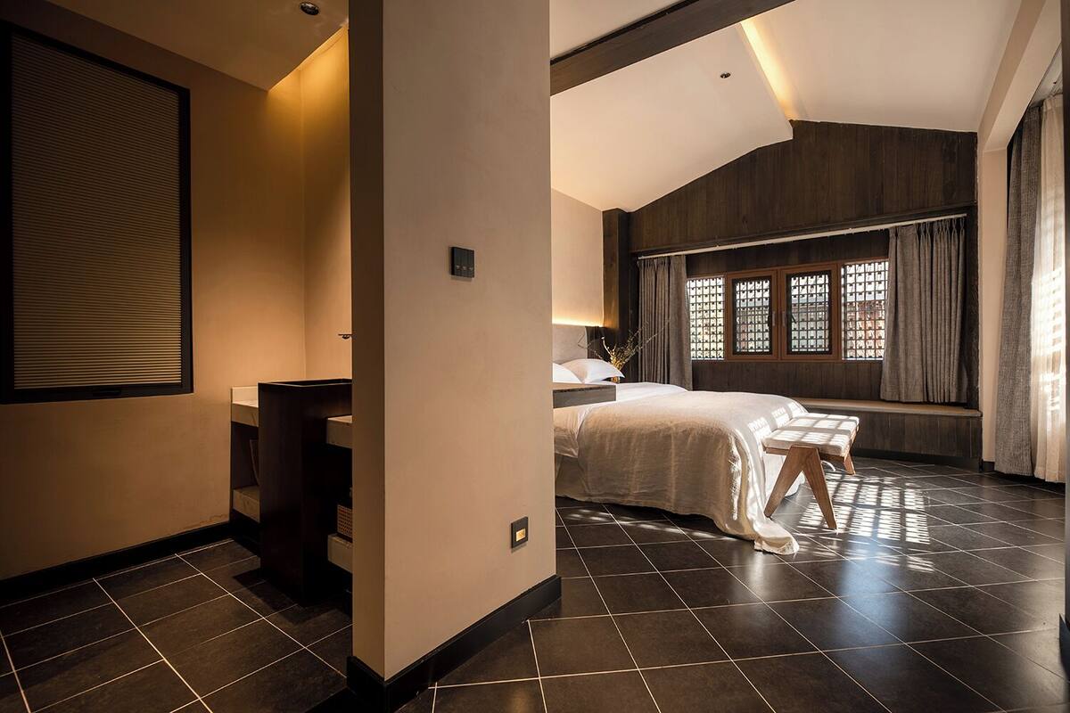 Ein Hotelzimmer mit Bett, Schreibtisch, einem Fenster mit Vorhängen und einem Fliesenboden.