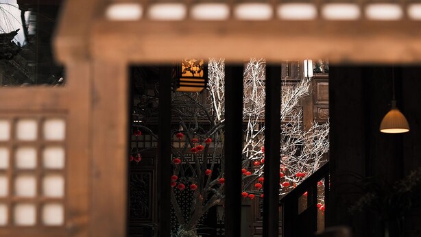 A traditional building with a window view of a tree adorned with red lanterns, wooden lattice structures, and a hanging light fixture. - Windy Wan Gang Wind Listening Art Hotel (Lijiang)