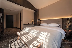 Una habitación de hotel moderna con una cama grande, un banco, una mesita de noche y una lámpara de pared.
