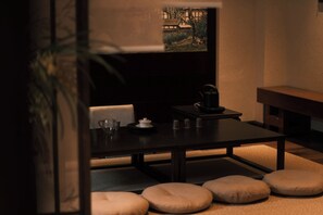 Una habitación tenuemente iluminada con una mesa dispuesta para el té, un cuadro en la pared y un sofá con cojines.