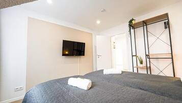 Een hotelkamer met twee bedden, een aan de muur bevestigde televisie en een kledingkast met schuifdeuren.