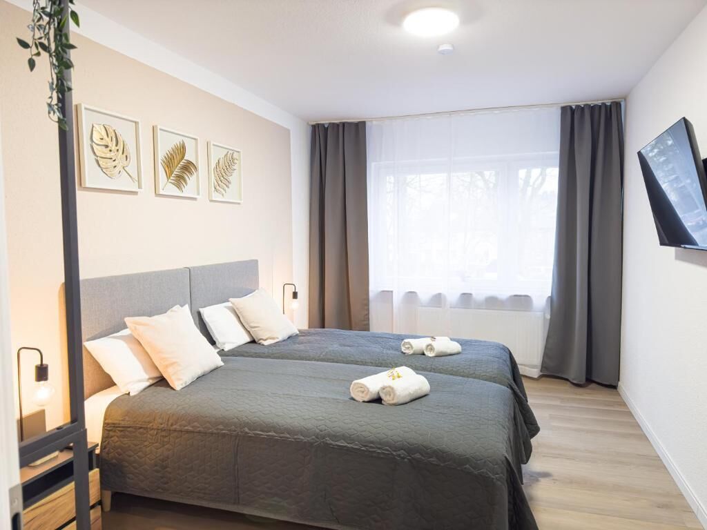 Une chambre d’hôtel avec deux lits, une grande fenêtre avec des rideaux, un téléviseur à écran plat et des œuvres d’art murales.