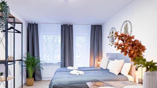 Habitación de hotel moderna con una cama grande, una mesita de noche, un pequeño escritorio, una planta en maceta y vistas al exterior.