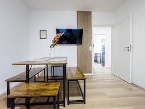 Una sala moderna con una mesa de comedor de madera, bancos, un televisor de pantalla plana y un panel de madera vertical.