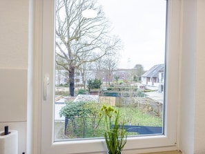 Una ventana con vistas a una zona residencial, un árbol y un pequeño jardín.