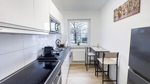 Una cocina moderna con armarios blancos, encimera negra, horno empotrado, refrigerador y ventana con vistas a árboles.