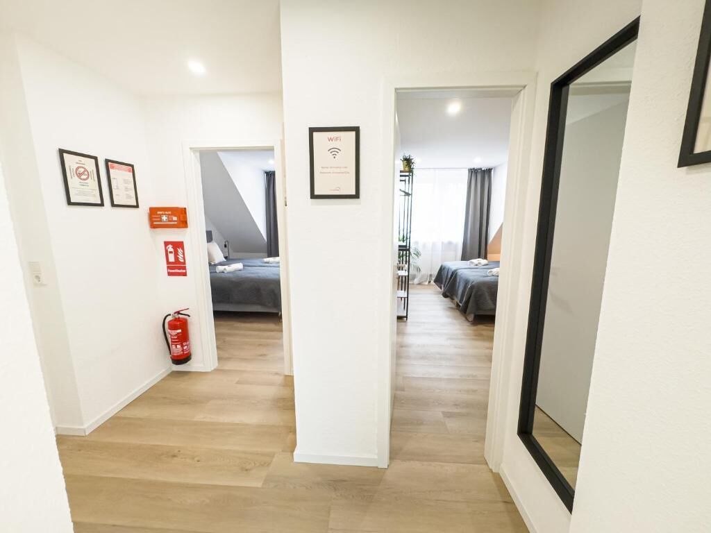 A corridor leading to a bedroom with a bed, a fire extinguisher, and a framed sign indicating WiFi availability.