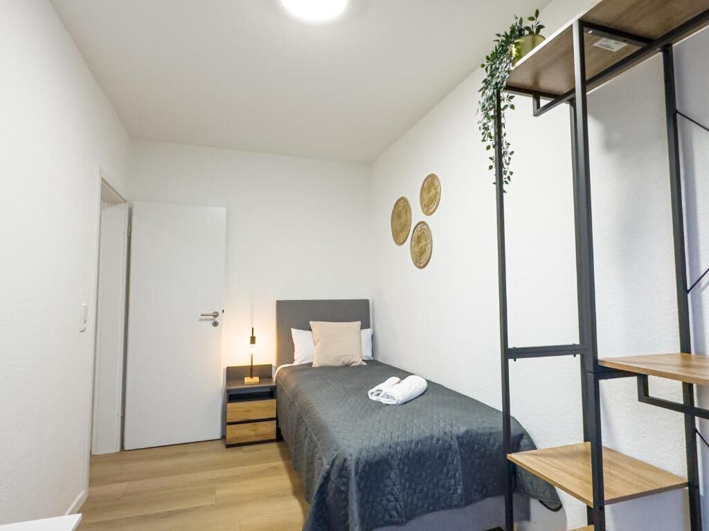 A compact bedroom with a bed, bedside table, and a small shelf unit.
