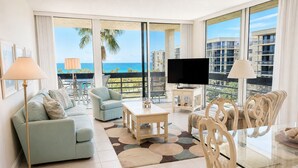 A modern living room with a sofa, armchair, coffee table, and TV, overlooking a balcony with a view of the ocean and buildings. - 2/2 Gulf View condo at Beachplace on Longboat Key (Longboat Key)
