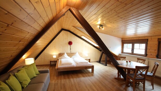 A loft-style room with a wooden ceiling, a bed with white linens, a green sofa, and a dining table with chairs. - Cozy Black Forest Studio (52 sqm) – Free Wi-Fi & Parking, Close to Town (Gengenbach)