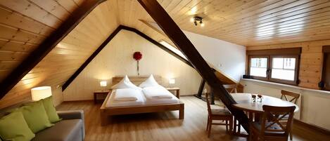 Una habitación estilo loft con techo inclinado, una cama, una mesa de comedor con sillas y un sofá.
