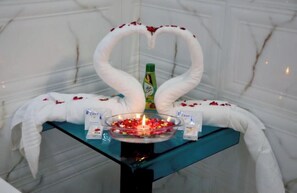 Ein Tisch mit einer herzförmigen Anordnung aus weißen Handtüchern, einer Haarpflegeflasche und einer Schale Rosenblätter.