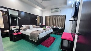 A modern hotel room with a bed, a desk, a chair, a mirror, and a TV. - Le-Leisure Hotel (Prayagraj)