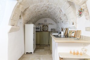 Cucina con arco in pietra, mobili bianchi, un piano di lavoro e uno scaffale con diversi oggetti.
