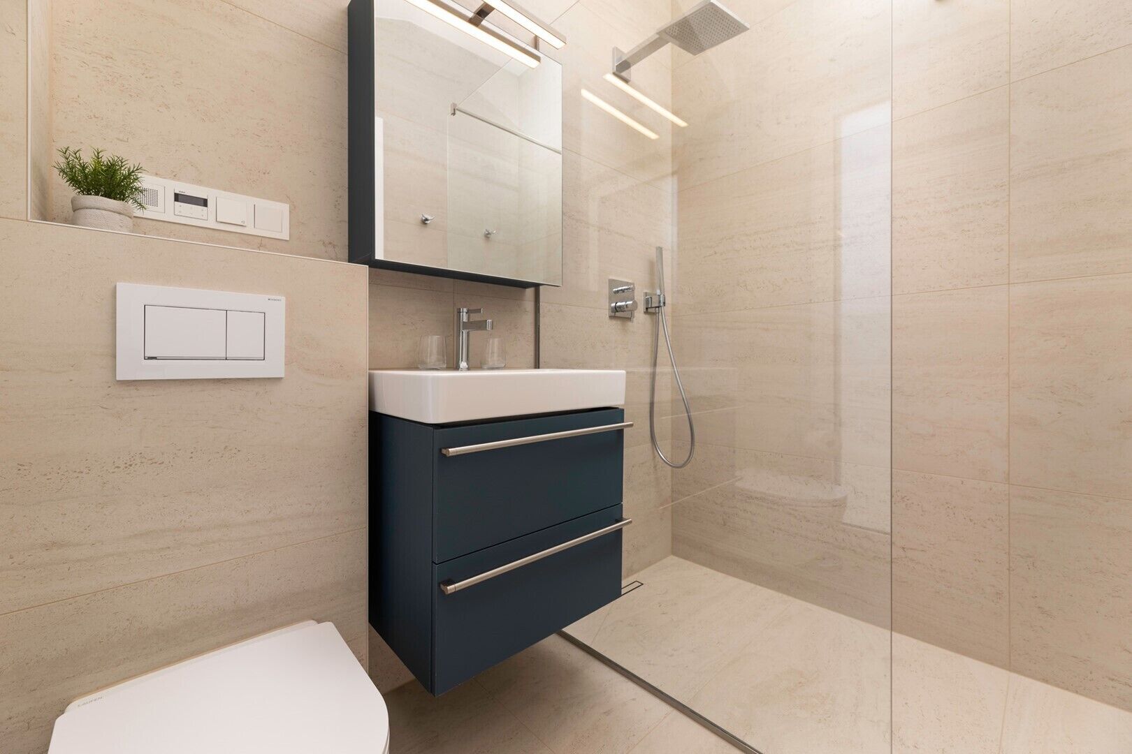Un baño moderno con inodoro, lavamanos con espejo, ducha y panel de control en la pared.