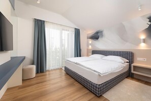 Ein modernes Hotelzimmer mit einem großen Bett, einem Flachbildfernseher, einem Fenster mit Vorhängen und einer Wandleuchte.