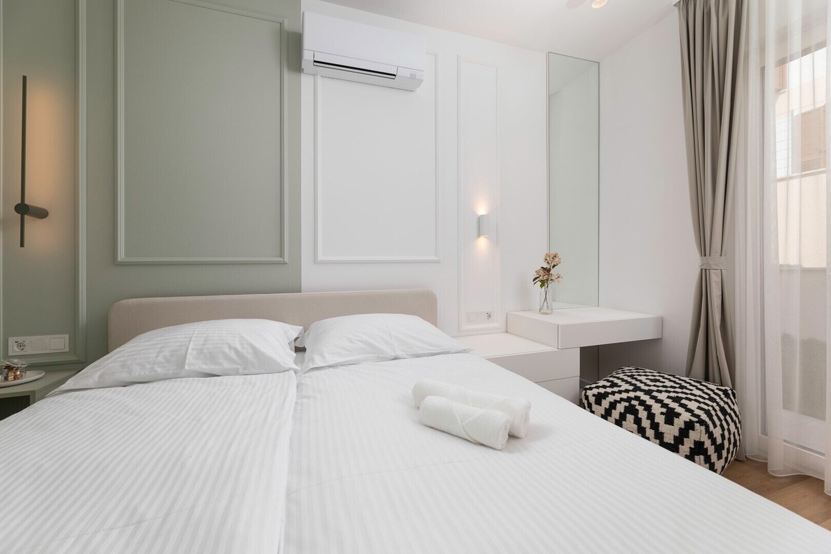 Moderni hotellihuone, jossa on suuri sänky, yöpöydät, peilipöytä ja ilmastointilaite.