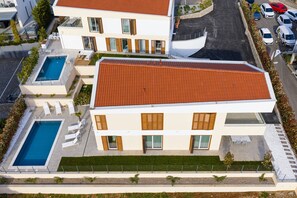 A modern two-story building with a swimming pool, outdoor seating, and a parking area. - Deluxe Olive Apartment with three bedrooms, swimming pool, and sea view – ground floor (Malinska)