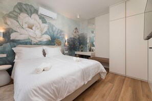 Ein modernes Schlafzimmer mit einem großen Bett, einer Wand-Klimaanlage, einem Nachttisch und einem Spiegel.