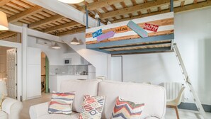 A modern living room with a sofa, decorative pillows, a wooden ceiling, and a visible staircase. - Apartment 'Casco Antiguo Sirocco' with Wi-Fi and Air Conditioning (Tarifa)