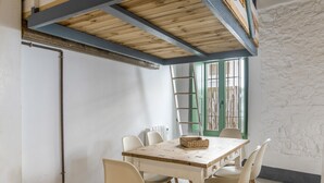 A dining area with a wooden table and chairs, a ladder, and a window with green shutters. - Apartment 'Casco Antiguo Sirocco' with Wi-Fi and Air Conditioning (Tarifa)