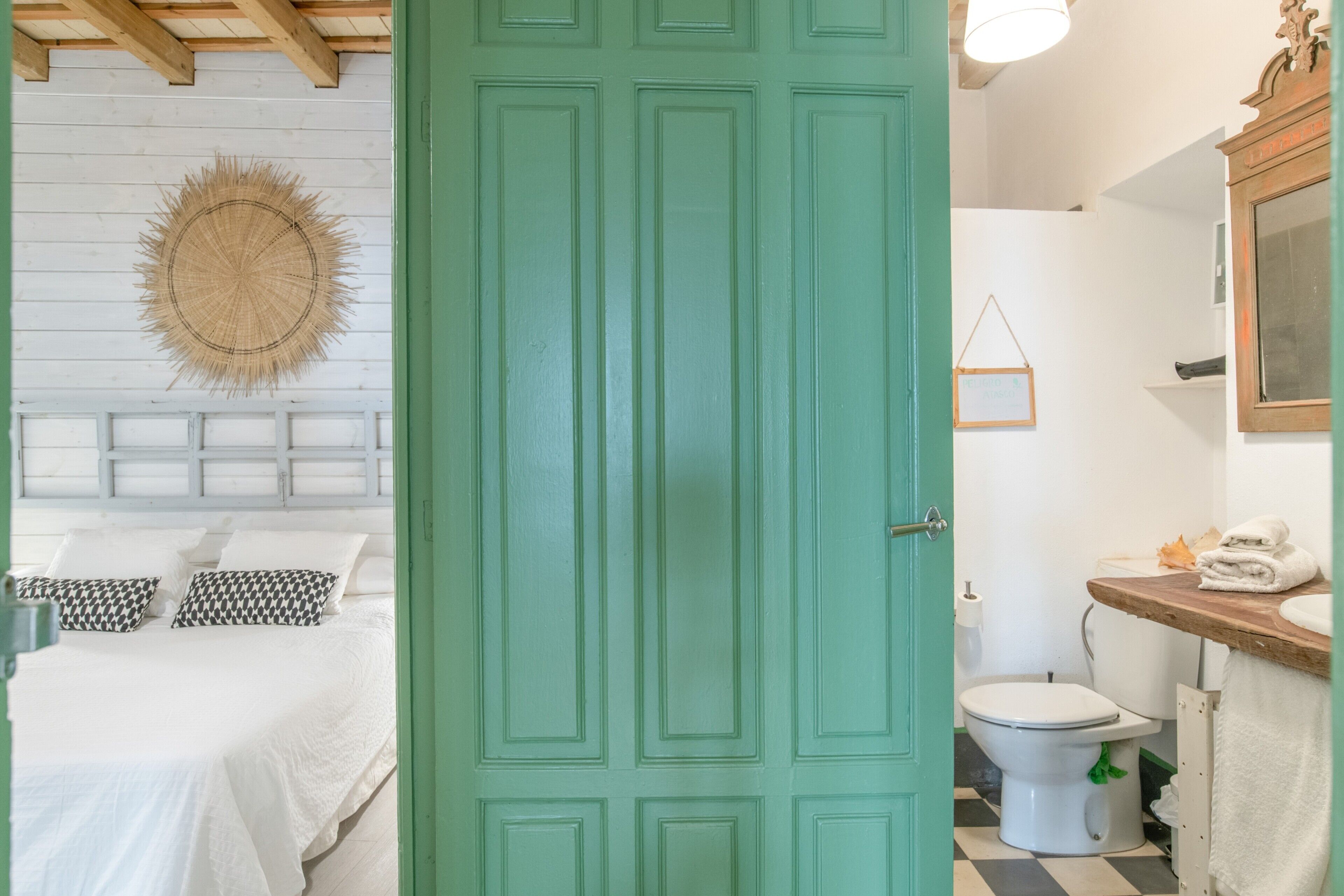 A room with a bed, a green door, a toilet, and a bathroom with a mirror and sink.